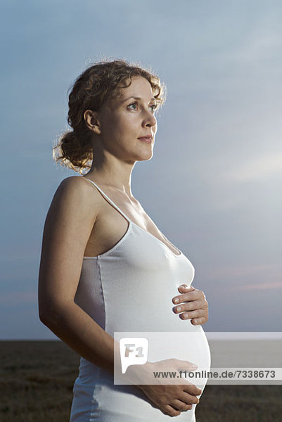 A pregnant woman holding her belly and looking away thoughtfully