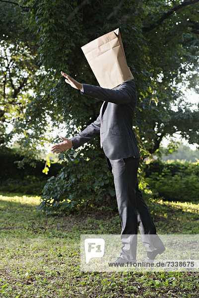 A businessman walking uncertainly with a paper bag on his head
