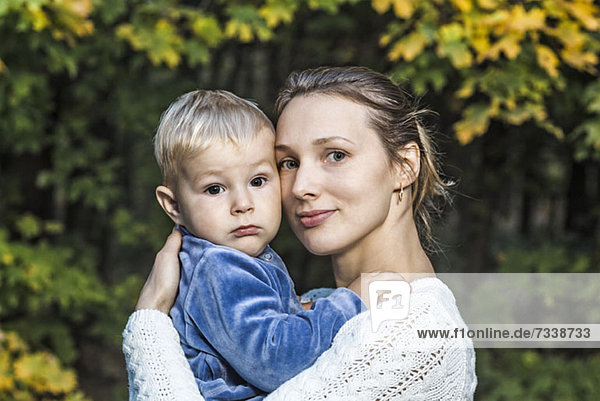 Eine junge Mutter hält ihren Sohn im Herbst in der Hand