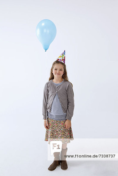 Ein Mädchen  das einen Partyhut trägt und einen Ballon hält.
