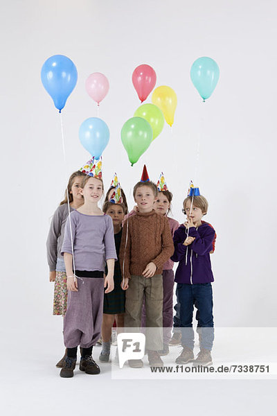 Eine Gruppe von Kindern trägt Partyhüte und hält Luftballons.