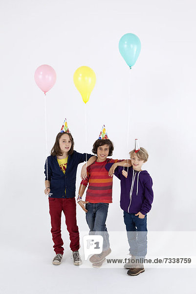 Drei Jungen mit Partyhüten und Luftballons in Folge