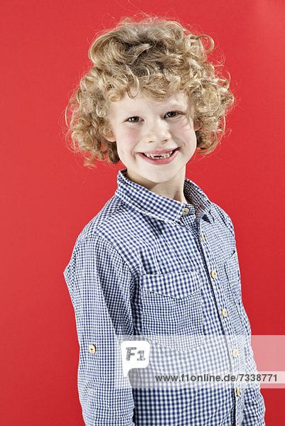 Ein Junge mit strubbeligen  lockigen  blonden Haaren  der die Kamera anlächelt.