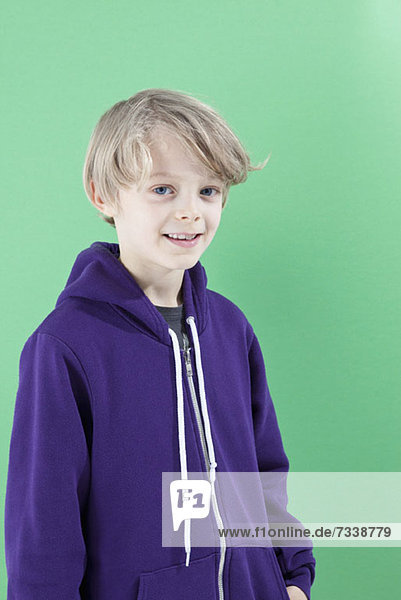 Ein Junge in einem lila Kapuzensweatshirt lächelt in die Kamera.