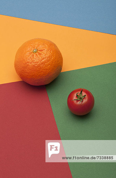 Eine Orange und eine Tomate auf einem mehrfarbigen  geometrischen Muster.