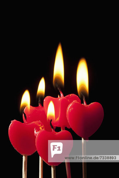 Fünf beleuchtete Kerzen in Herzform auf Stäbchen in einer Gruppe angeordnet