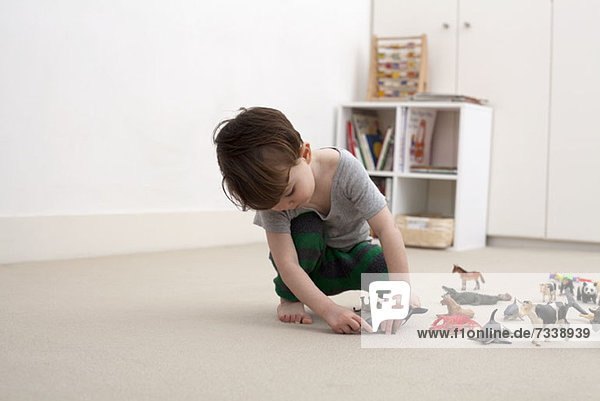 Ein kleiner Junge spielt mit ein paar Spielzeugtierfiguren auf dem Boden seines Schlafzimmers.