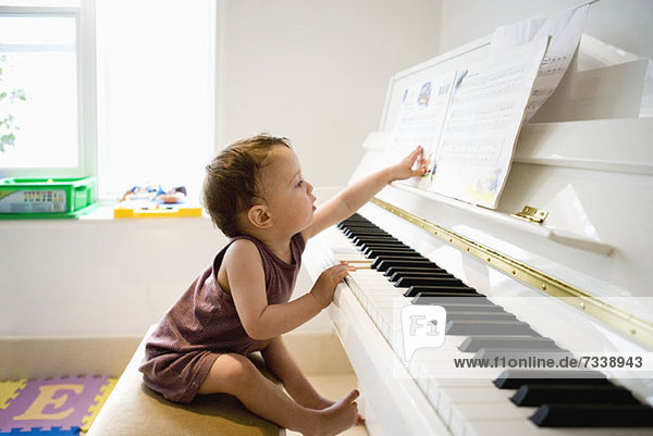Ein kleiner Junge sitzt am Klavier und greift neugierig nach den Noten.