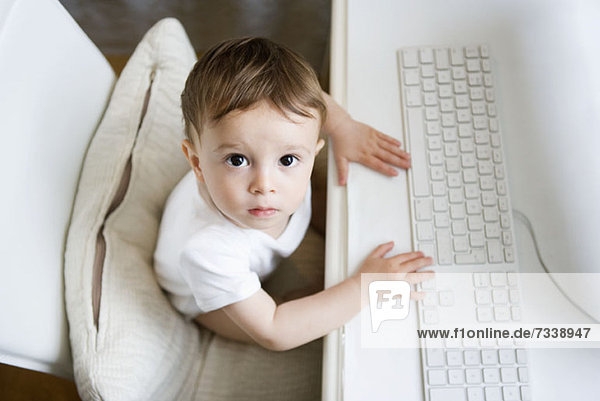 A toddler sitting at a desk with a computer keyboard