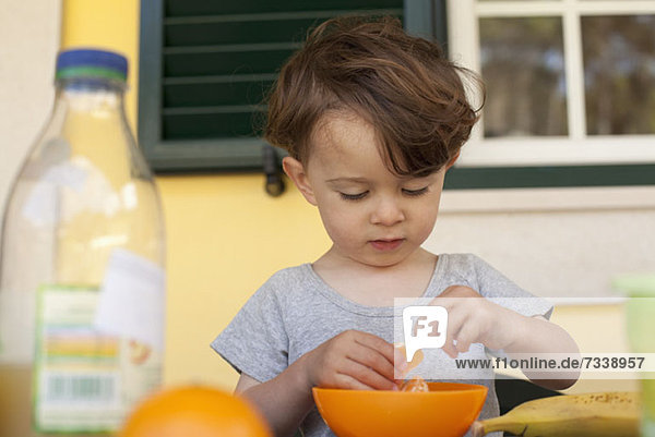 Ein Junge bereitet sich darauf vor  eine Scheibe frische Orange zum Frühstück zu essen.