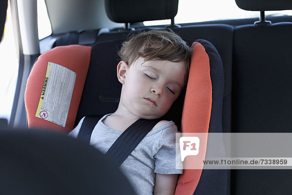 Ein Junge schläft in einem Autositz auf dem Rücksitz eines Autos.