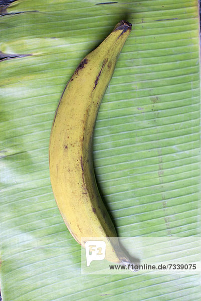 A banana lying on a banana leaf