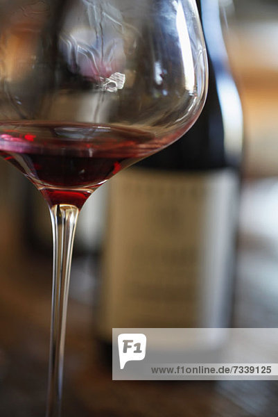 Ein Weinglas mit Rotwein und zwei Flaschen Wein im Hintergrund