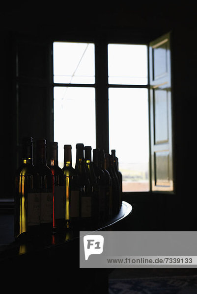 A row of various wine bottles on a bar counter near an open window