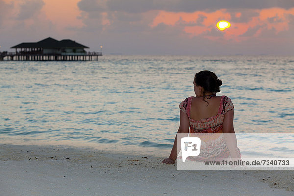 Ein Mädchen  etwa 15 Jahre  schaut vom Strand aus auf den Sonnenuntergang  Nord-Male-Atoll  Republik Malediven  Indischer Ozean  Asien