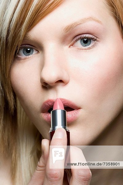 Portrait of a young woman applying lipstick