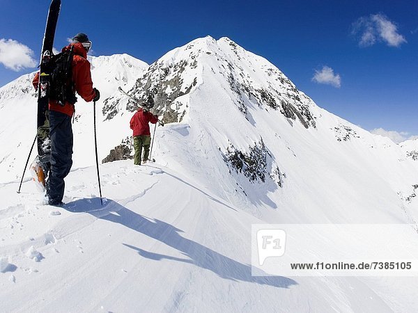 Rear view of two people with ski poles and snowboard on snowy mountain