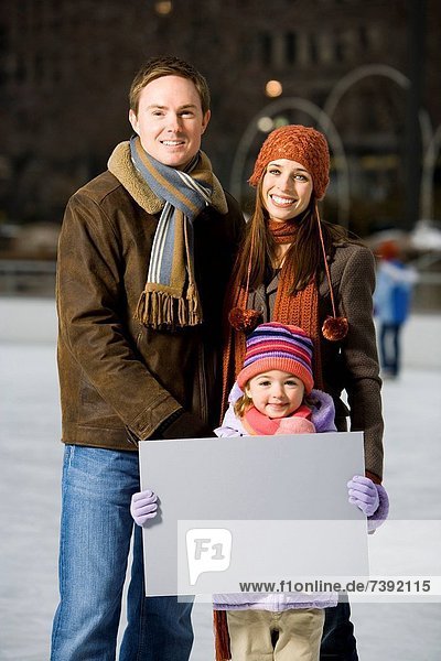 Man and woman with girl holding blank sign outdoors in winter