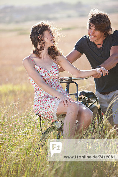 Couple playing on bicycle in tall grass