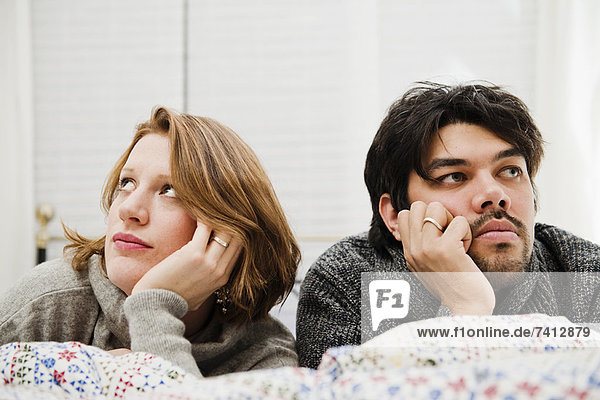 Couple resting chins in hands on bed