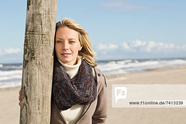Woman leaning on pole on beach