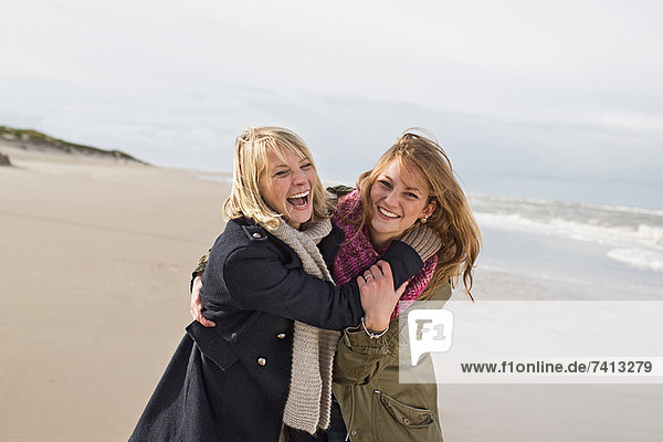 Lächelnde Frauen  die sich am Strand umarmen