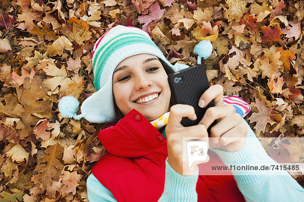 Young woman lying on autumn leaves and using