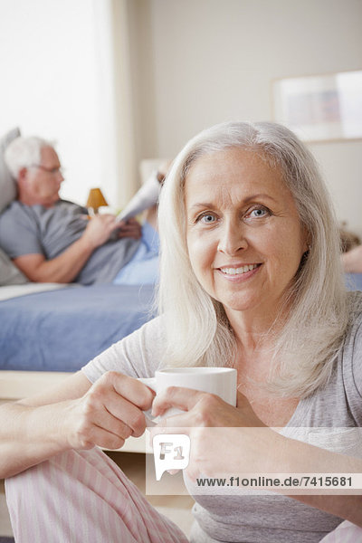 Senior woman holding mug  man sitting on bed in background