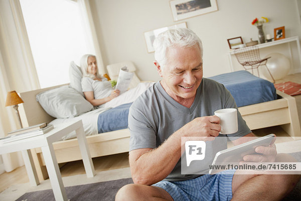 Senior man holding mug  woman sitting on bed in background