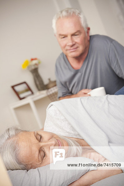 Senior man with coffee cup looking at sleeping wife