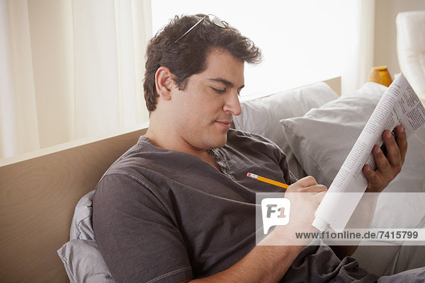 Young man laying on bed filling crossword