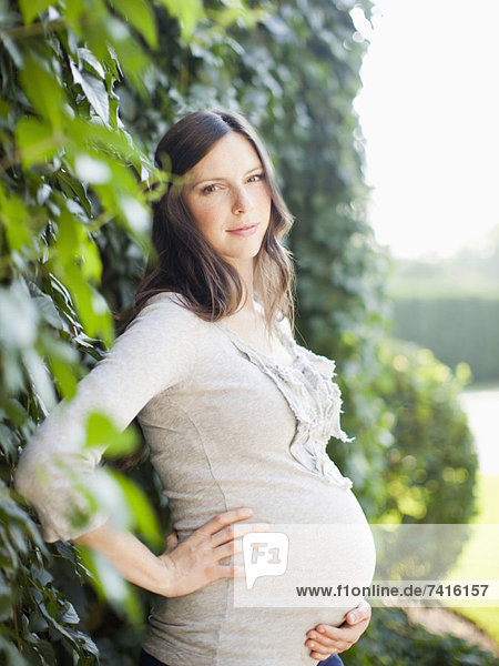 Portrait of pregnant mid adult woman next to hedge