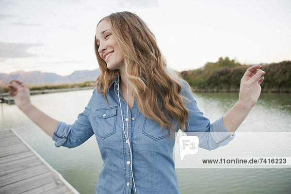 Portrait of young woman listening to mp3 player on jetty