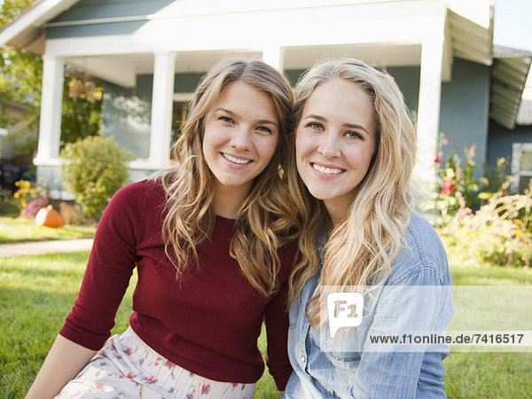 Portrait of two young women cheek to cheek in front of house