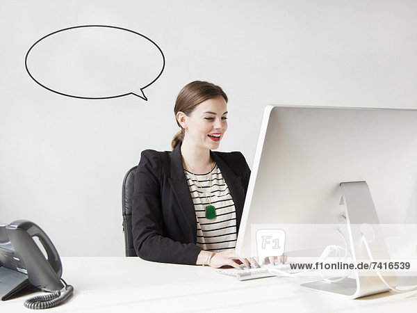 Studio shot of young woman working on computer with speech bubble next to her head