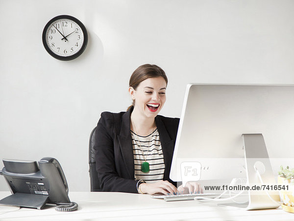 Studio shot of young woman working on computer and laughing