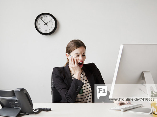Studio shot of young woman working in office yawning