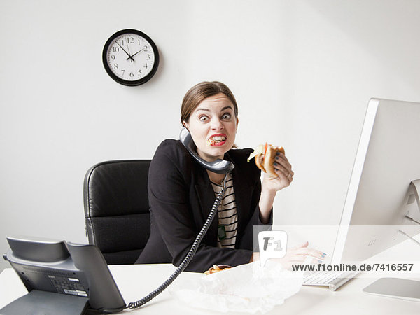 Studio shot of young woman working in office and having lunch same time