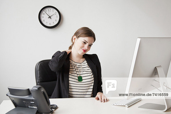 Studio shot of young woman working in office and touching her neck