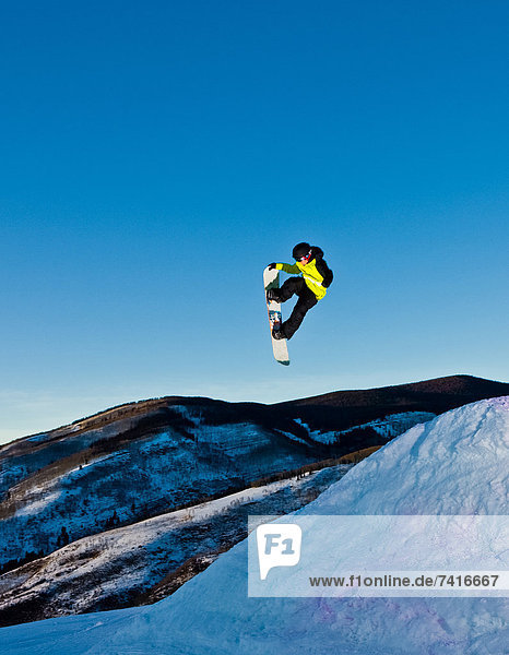 A snowboarder launches into the twilight sky.