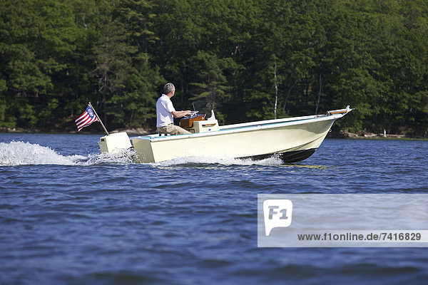 A middle-aged man drives his newly restored power boat along the scenic coast of Maine.