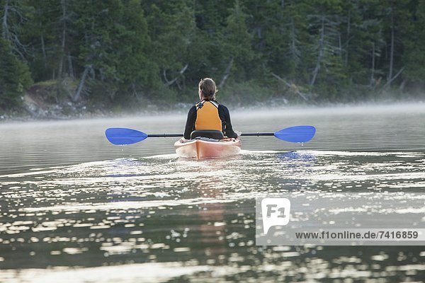 Rear view of a woman sitting in a kayak on Spencer Pond  in Maine.