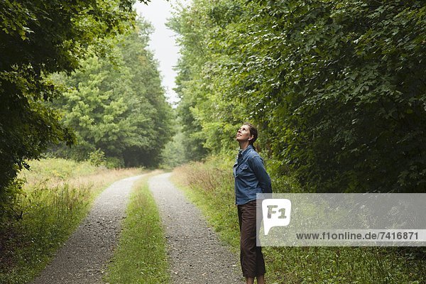 A woman standing in a clearing on an empty road in the woods of northern Maine  near Spencer Pond.