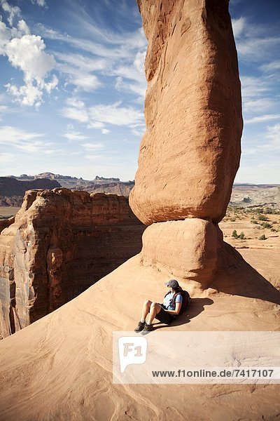 A female hiker rests against Delicate Arch in Arches National Park  Utah.