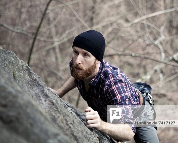 A male rock climber with a beard scales the side of a cliff.