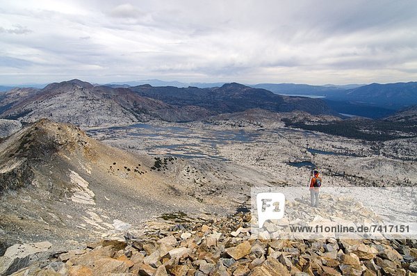 A male hiker looks over Lake Aloha  Desolation Wilderness and Lake Tahoe from the summit of Pyramid Peak  CA.