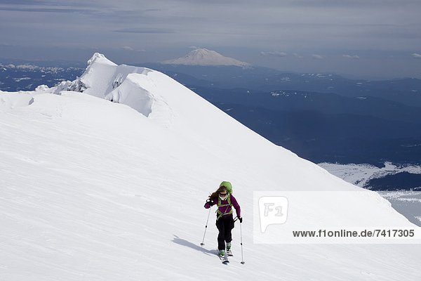 A skier traverses a steep slope while climbing a mountain on a snowy day in the Cascades.