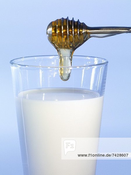 Honig tropft in ein Milchglas