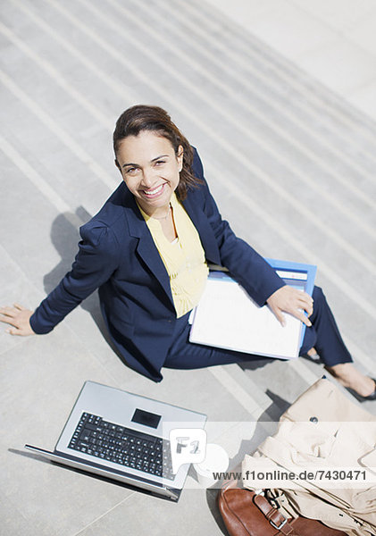 Portrait of smiling businesswoman with paperwork  coffee and laptop on steps