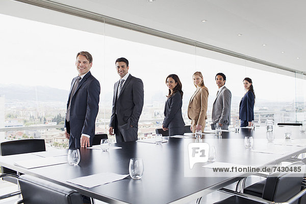 Porträt von lächelnden Geschäftsleuten  die in einer Reihe am Fenster des Konferenzraums stehen.